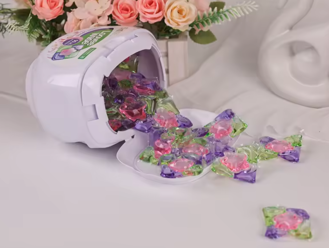 Tipped tub of Flower Pod laundry pods in Velvet Garden spilling pods onto a white surface with roses behind