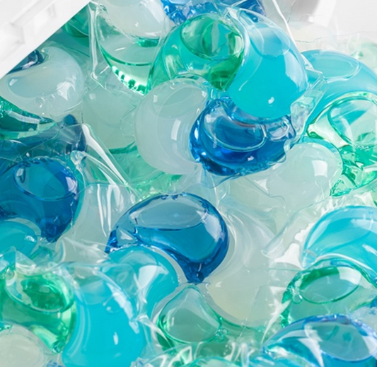 Close-up of blue, teal and green Swirl Pod laundry pods filling a container